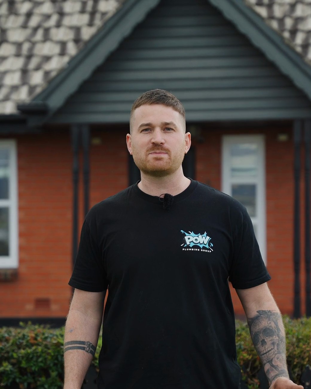 Brandon Ellis in a black POW Plumbing Group t-shirt outside a red brick house
